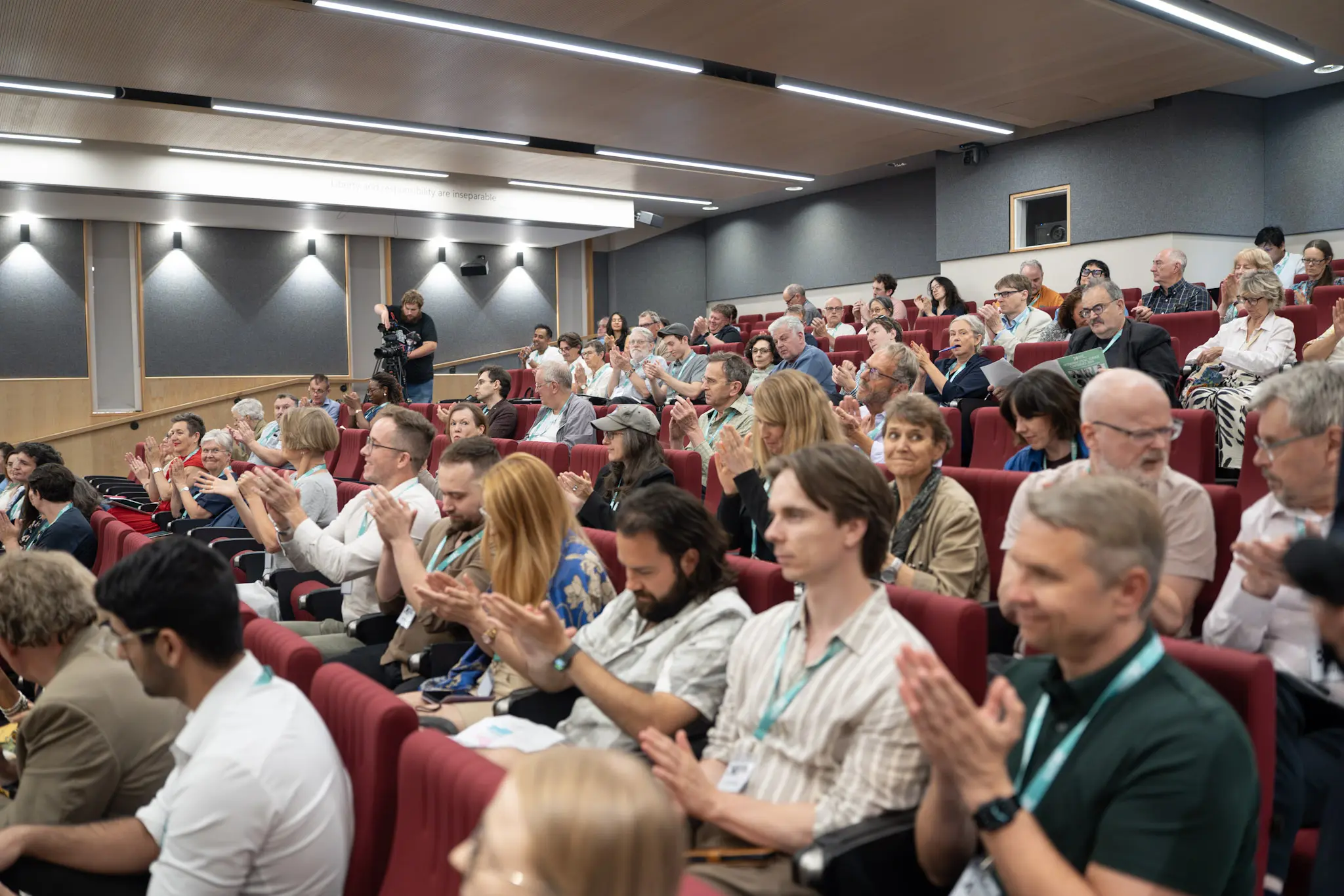 Delegates seated in a tiered auditorium applauding during the Heterodox Conference